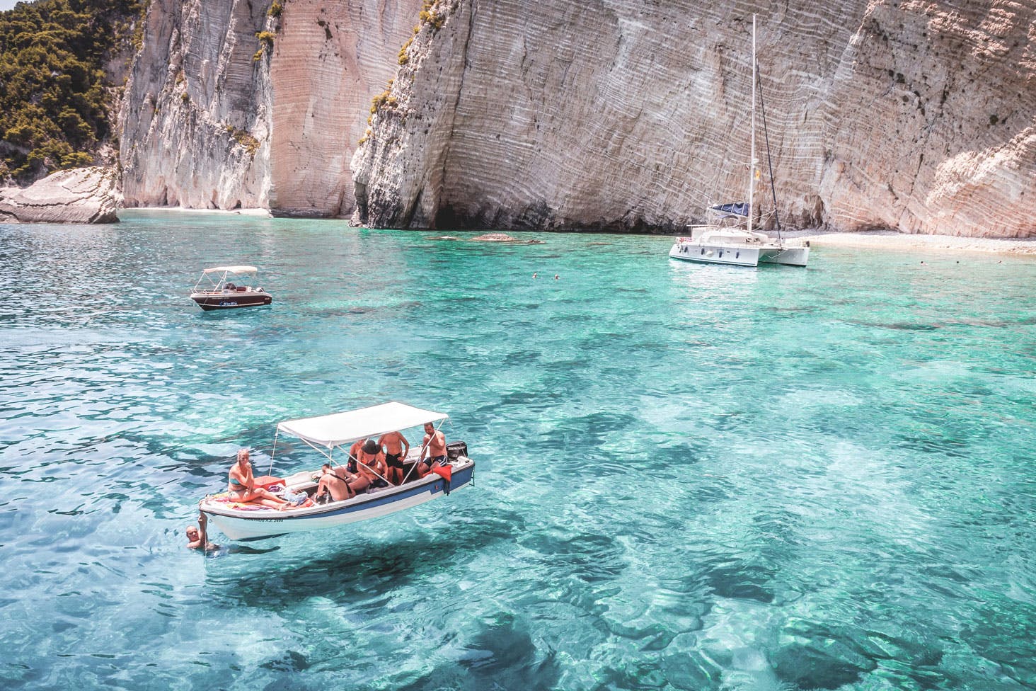 a boat floating near a white cliff in bright blue water
